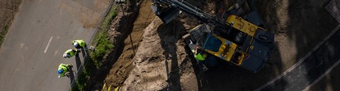 Aerial view of the construction site with a total of four Oulun Energia employees and an excavator. Employees are wearing their work gear.