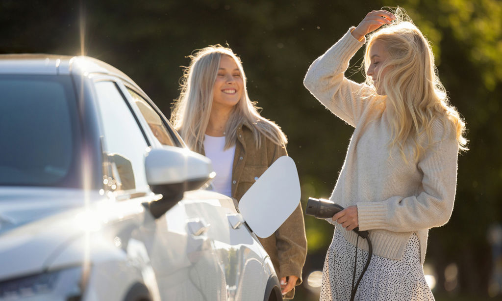 Two persons are charging an electric car in a sunshine. 