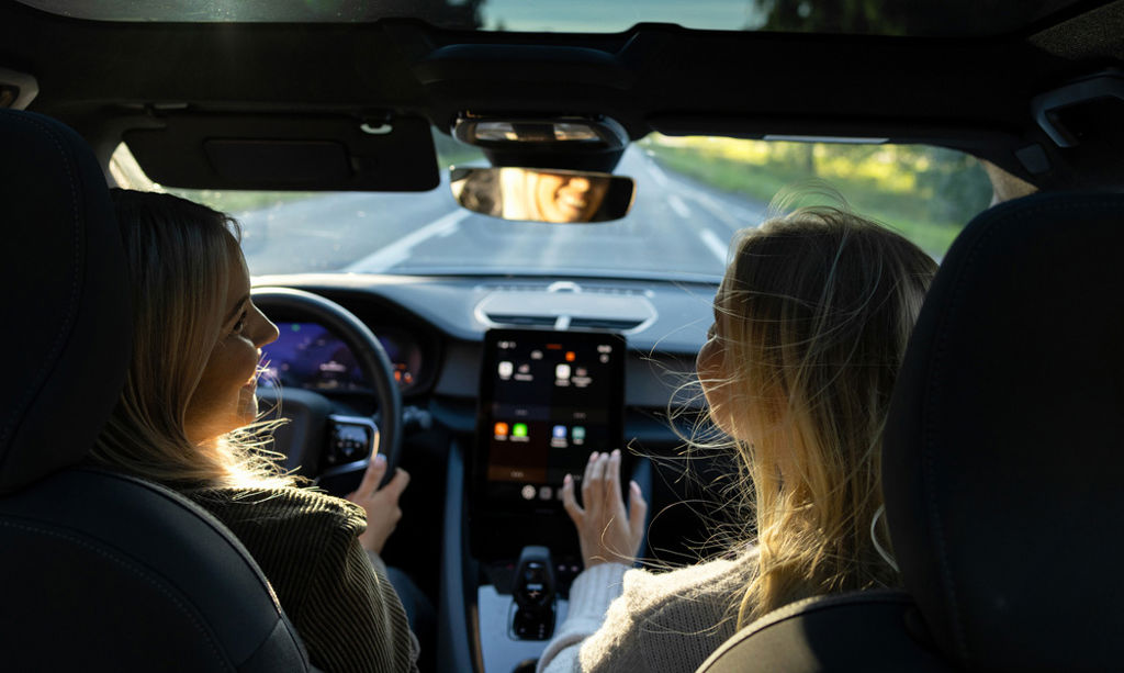 Two persons are driving an electric car. Driver's smile reflects from the rear-view mirror. 