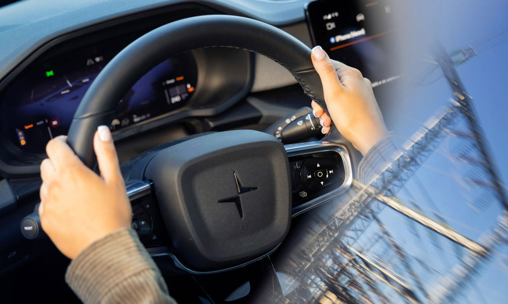 A person is holding electric car's wheel. There is a reflection of an electric power plant on the car's window.  
