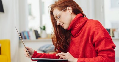 Punatukkainen tyttö silmälasit päässä selailee läppäriä.