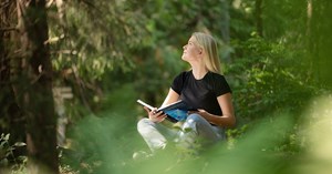 Nuori ihminen lukee kirjaa metsässä ja katsoo toivekkaasti kohti taivasta.