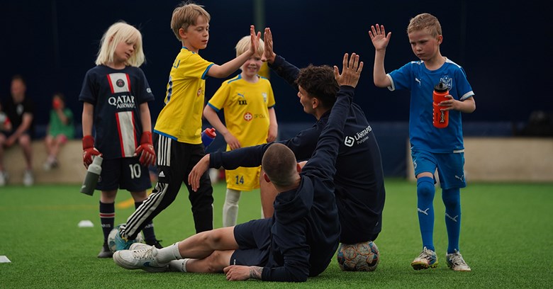 AC Oulun pelaajat makaavat Garam Masalan tekonurmella ja lyövät käsiään yhteen lasten kanssa.