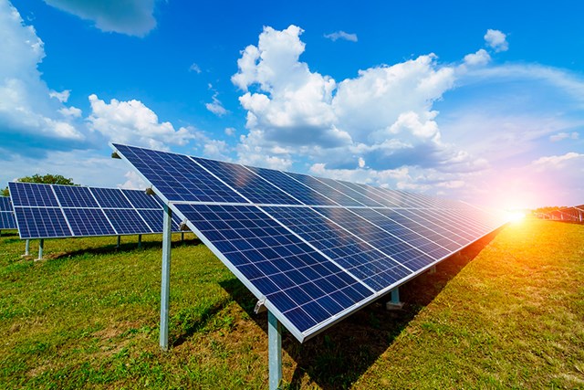 Solar panels are placed on the lawn, and the sun shines behind them.