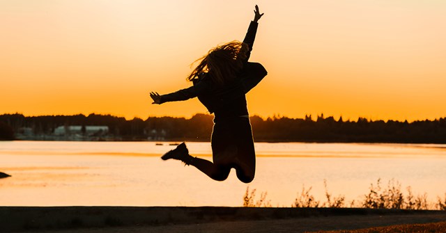 A woman is jumping at a beach during a sunset.