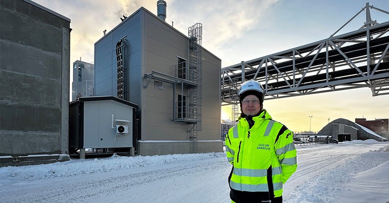 Lauri Heilala seisoo ja hymyilee Sähkökattila hänen selkänsä takana.