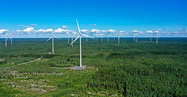 The aerial image shows wind turbines in a Finnish forest landscape.