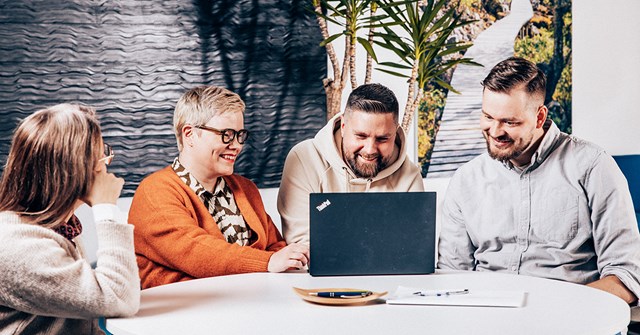 Neljä Oulun Energian työntekijää istuvat hymy huulilla pöydän ääressä, yhden edessä on läppäri.