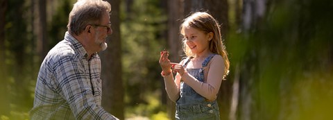 Grandfather and grandson are in the forest. The girl is holding and showing her grandfather a cone she has found.