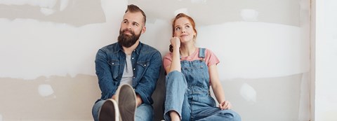 Punatukkainen nainen ja tummatukkainen mies istuvat lattialla ja nojaavat seinään.