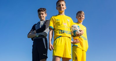  Three young soccer players stand proudly on the field.