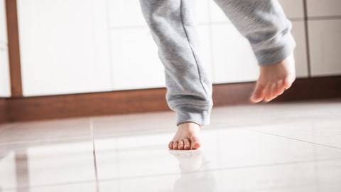 The feet of a running toddler on a tiled floor.