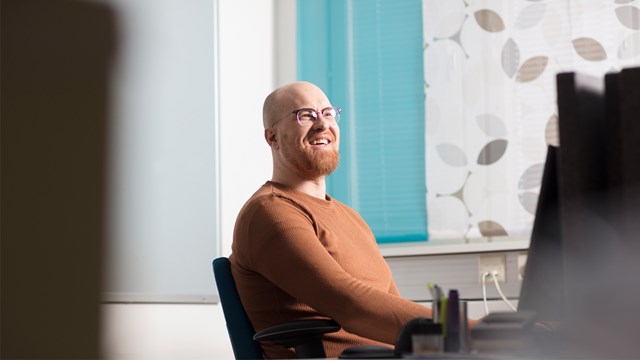 Oulun Energian työntekijä istuu tietokoneen edessä ja hymyilee leveästi.
