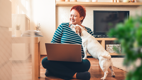 A woman is sitting on the floor and a dog is licking her face.