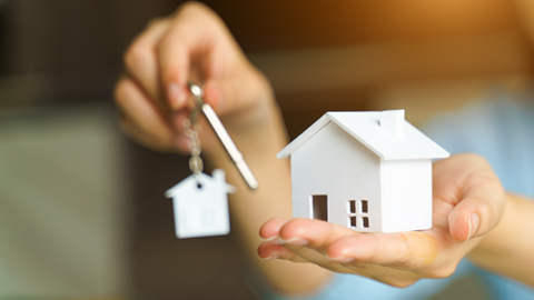 The person is holding a small white toy house in his right hand. In his left hand he is holding a key.